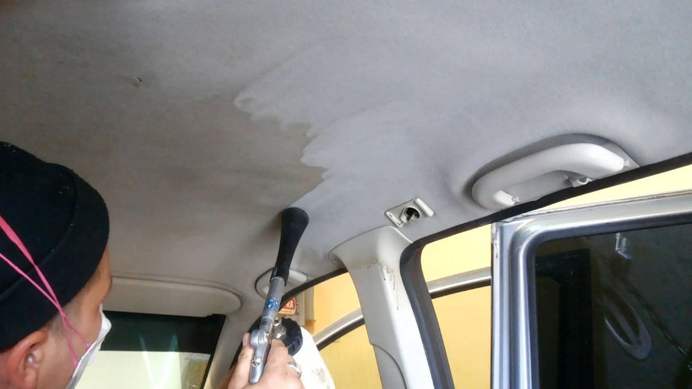 Мужчина делает химчистку потолка в автомобиле
